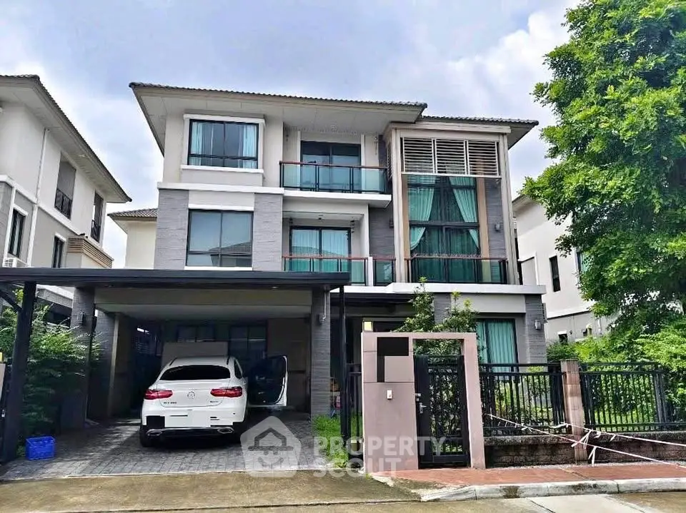 Modern three-story house with carport and lush greenery in a serene neighborhood.