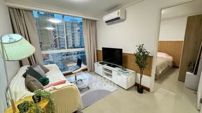 Modern living room with cozy decor and large window view, adjacent to a stylish bedroom.