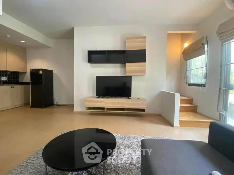 Modern living room with sleek furniture and open kitchen layout, featuring a stylish TV unit and cozy ambiance.