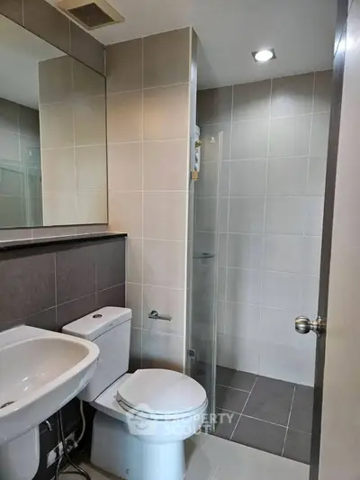 Modern bathroom with sleek design and neutral tiles, featuring a glass shower enclosure and contemporary fixtures.