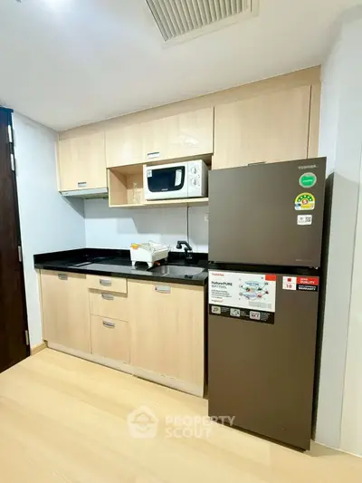 Modern kitchen with sleek cabinets, microwave, and fridge in a compact layout.