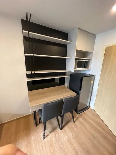 Modern kitchen with sleek shelving, compact fridge, and dining area in stylish apartment.