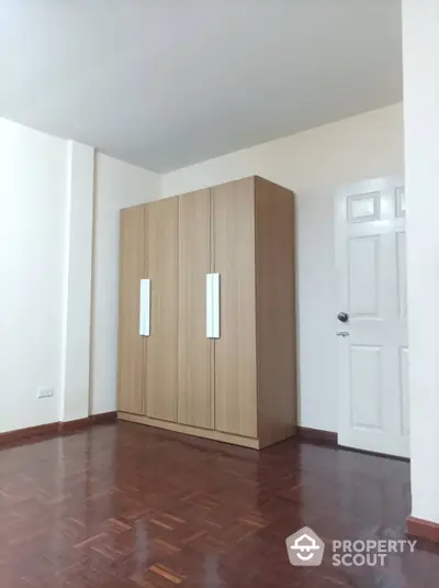 Spacious and bright bedroom with polished hardwood floors and a large built-in wooden wardrobe, offering ample storage space and a clean, modern aesthetic.