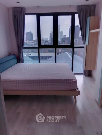 Modern bedroom with city view and large windows, featuring a cozy bed and stylish decor.