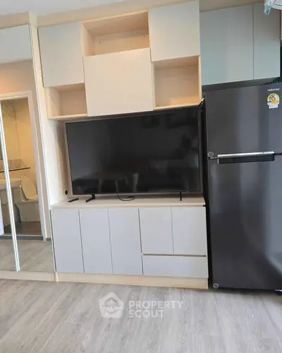 Modern living room with sleek TV unit and stainless steel fridge, showcasing contemporary design and functionality.