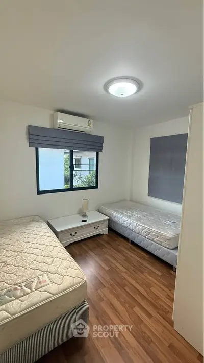 Cozy bedroom with two beds, wooden flooring, and natural light from window.