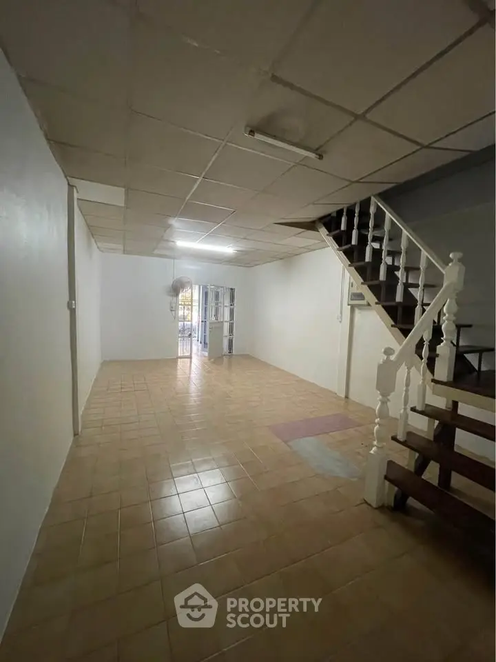 Spacious empty room with tiled floor and staircase, ideal for customization.