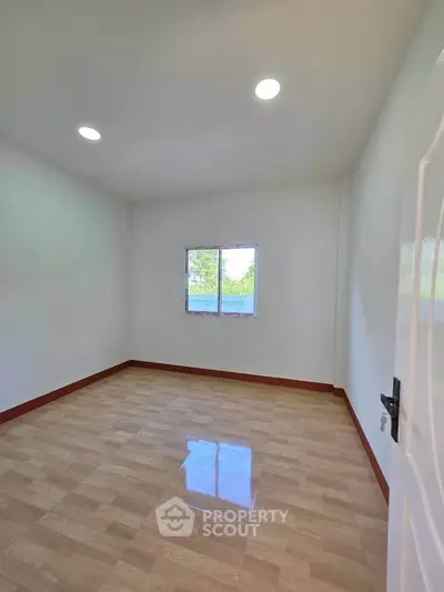 Spacious empty room with polished wooden floor and bright window view.