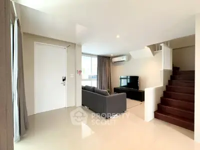 Spacious modern living room with sleek design and staircase, perfect for family gatherings.