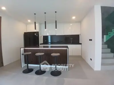 Modern kitchen with sleek black and white design, featuring an island and stylish lighting.