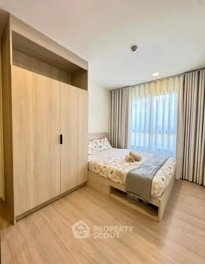 Modern bedroom with wooden flooring, large window, and stylish wardrobe in a cozy apartment.