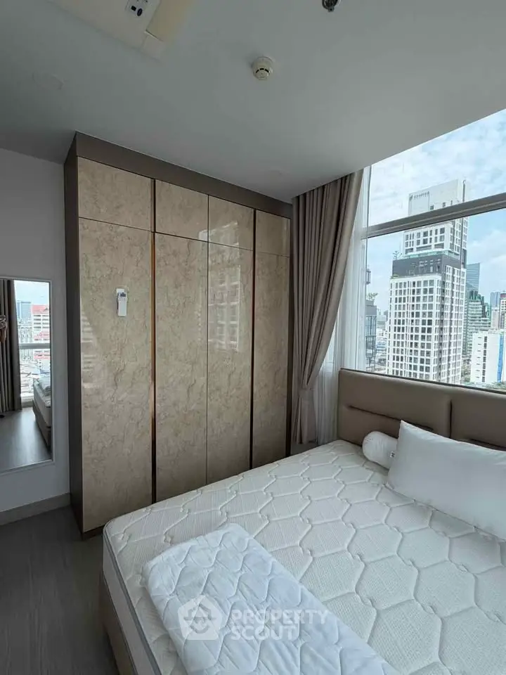 Modern bedroom with large window offering city view, featuring a comfortable bed and sleek wardrobe.