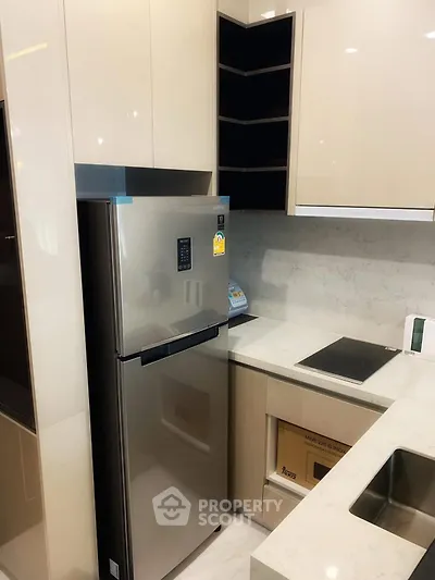 Modern kitchen with sleek cabinets and stainless steel fridge in compact layout.