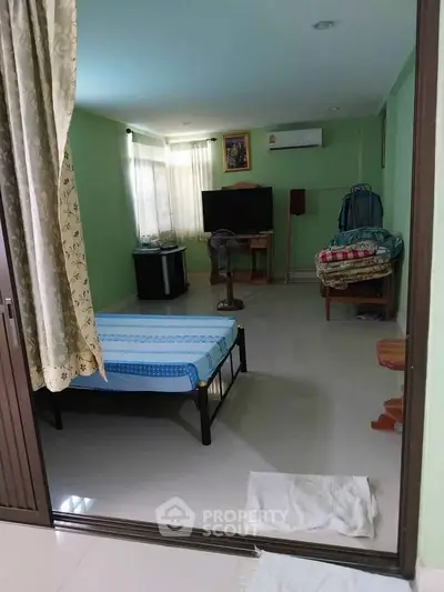 Spacious bedroom with green walls, featuring a bed, TV, and air conditioning.
