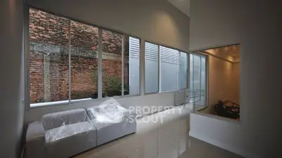 Modern interior with large windows and sleek design, featuring a wrapped sofa and brick wall view.