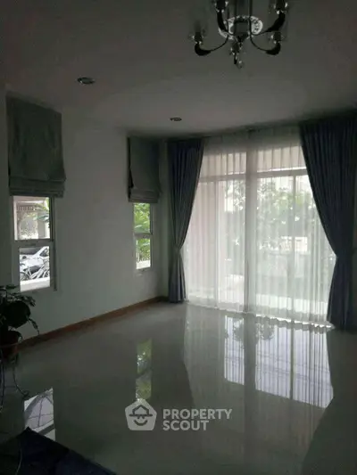 Spacious living room with large windows and elegant curtains, offering abundant natural light and serene garden views.