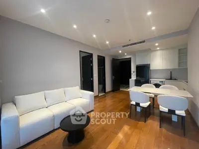 Modern living room with sleek furniture and open kitchen layout, featuring hardwood floors and elegant lighting.