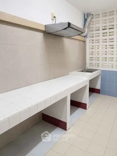 Spacious kitchen with tiled countertops and modern ventilation system, perfect for culinary enthusiasts.