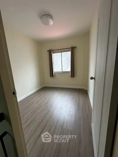 Spacious empty bedroom with wooden flooring and natural light from window.