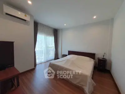 Spacious bedroom with wooden flooring and natural light