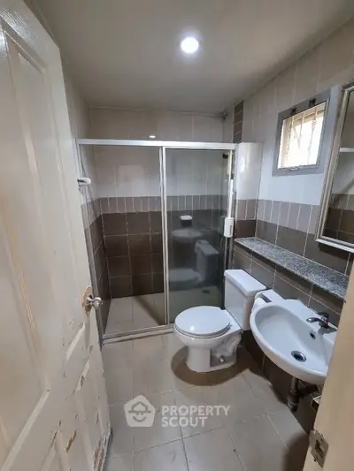 Compact bathroom with glass shower, toilet, and sink in neutral tones.