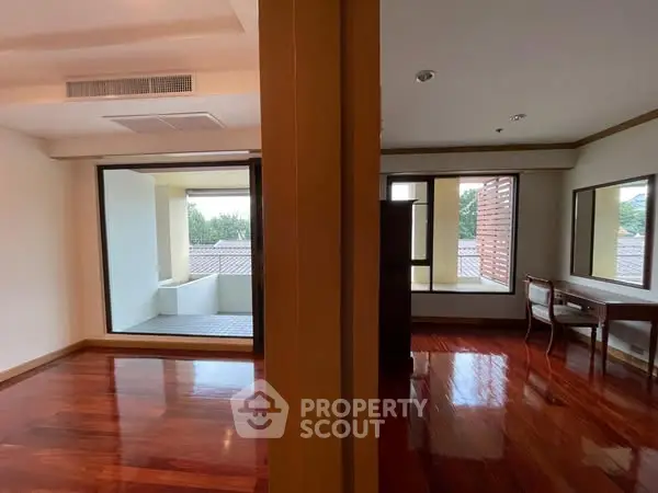 Spacious room with wooden floors and large windows offering natural light and outdoor views.