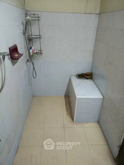 Simple bathroom with tiled walls and shower area, featuring a small bench for convenience.