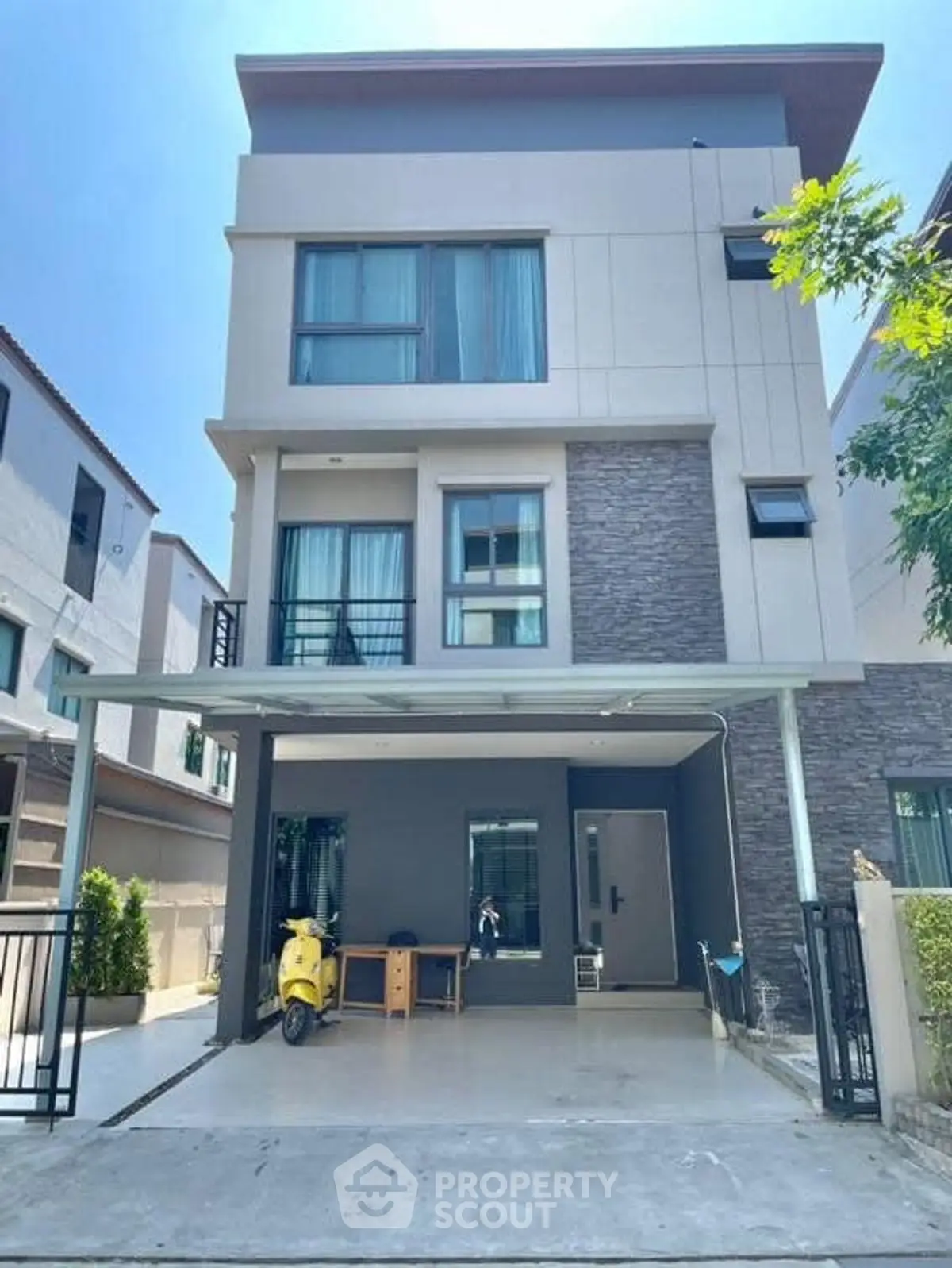 Modern three-story house with spacious driveway and sleek facade in a suburban neighborhood.