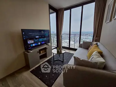 Modern living room with large windows and city view, featuring a sleek TV setup and cozy seating area.