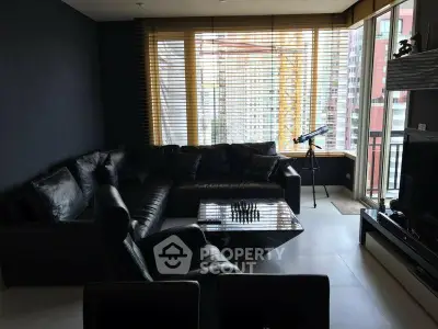 Modern living room with black leather sectional, chessboard, and telescope by large windows.