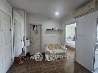 Cozy apartment interior with wooden flooring and air conditioning, featuring a small sofa and a glimpse of a bedroom.