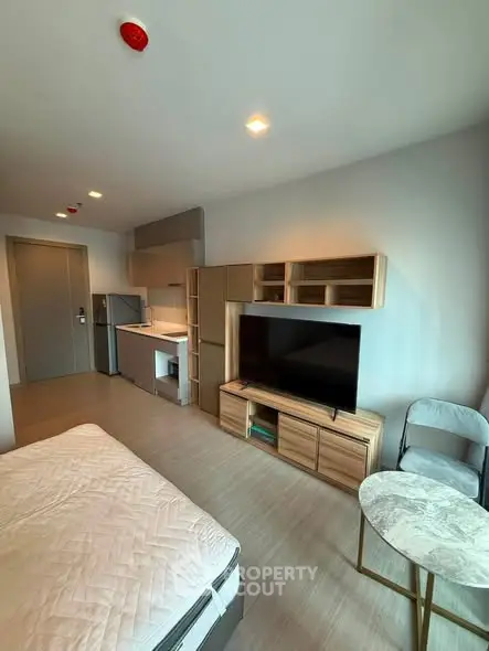 Modern studio apartment with compact kitchen and cozy living area, featuring stylish furniture and natural lighting.