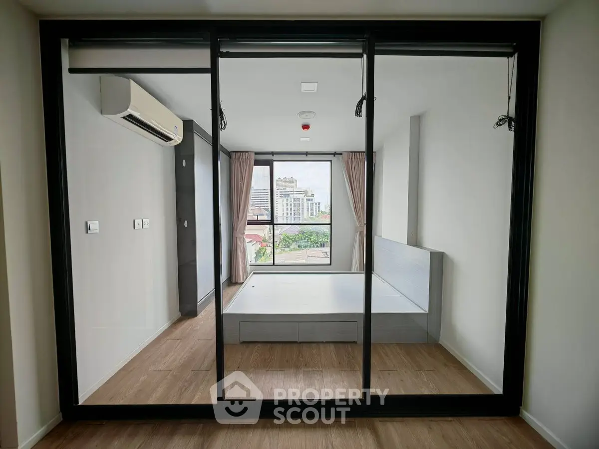 Modern bedroom with large window and city view, featuring sleek design and wooden flooring.
