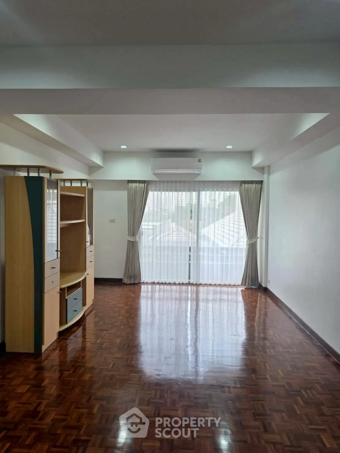 Spacious living room with polished wooden floors and large window for natural light.