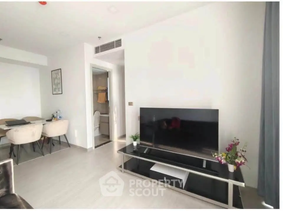 Modern living room with sleek TV setup and dining area in open layout apartment.