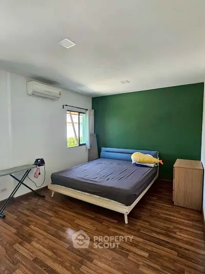 Spacious bedroom with modern decor and wooden flooring, featuring a comfortable bed and air conditioning.