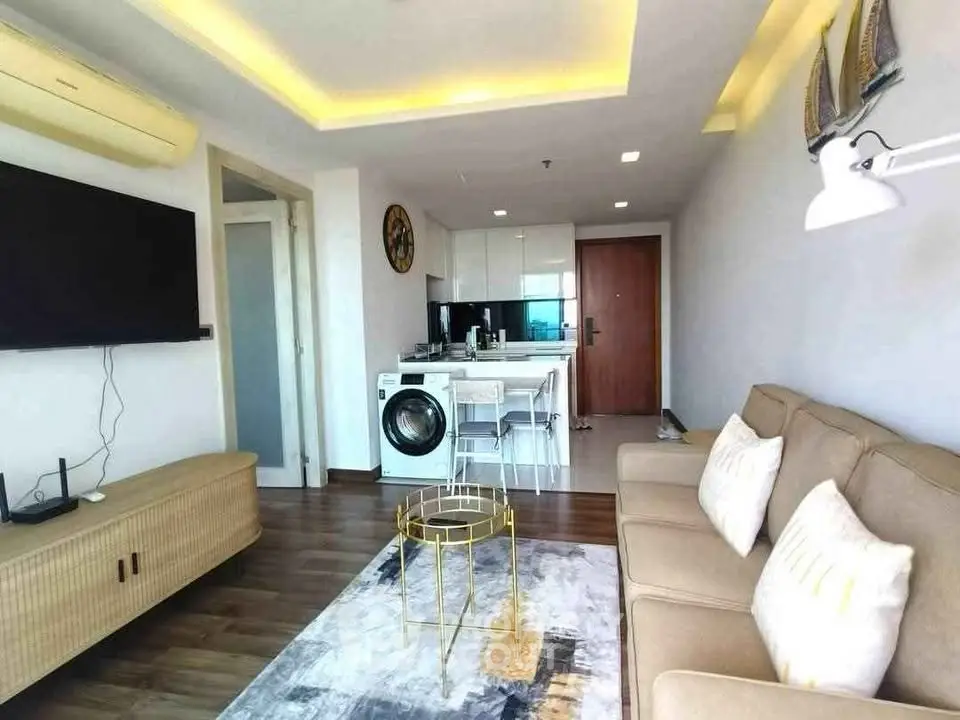 Modern living room with open kitchen and washing machine, featuring stylish decor and cozy seating.