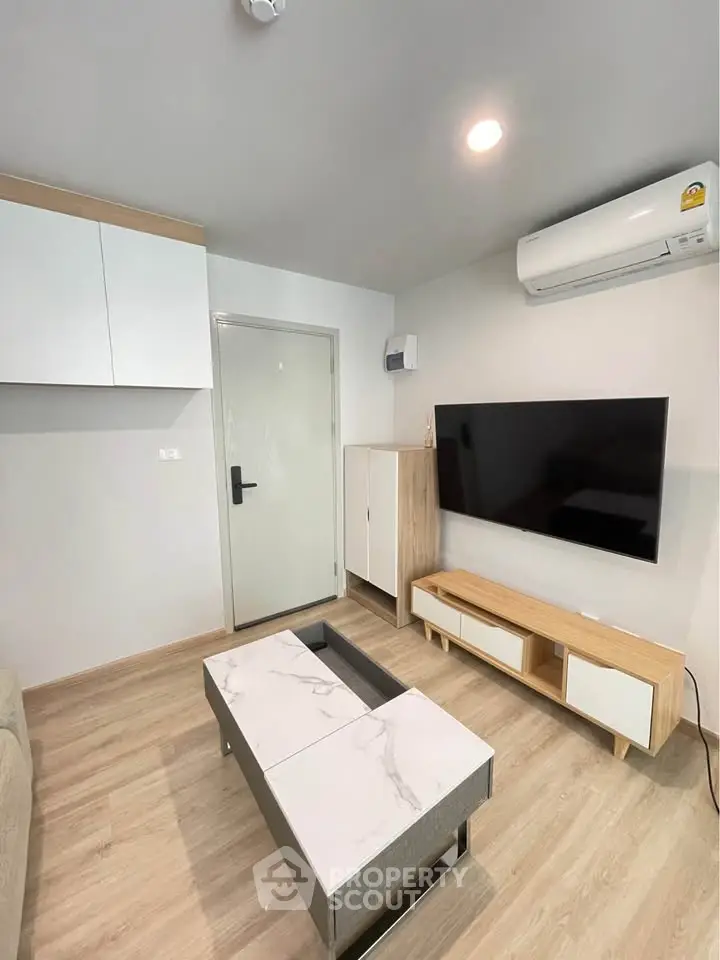 Modern living room with sleek furniture and wall-mounted TV, featuring a minimalist design and air conditioning.