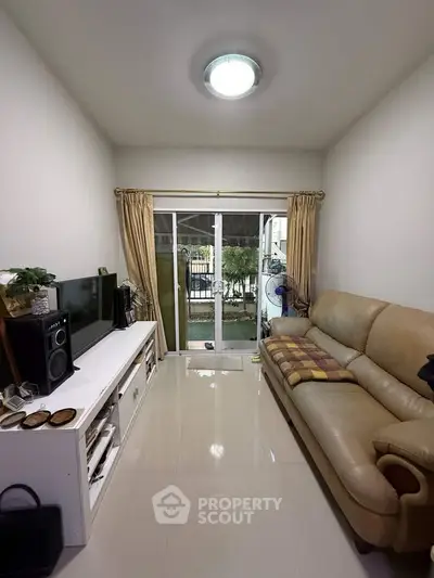 Cozy living room with leather sofa and entertainment center, featuring sliding glass doors to outdoor view.