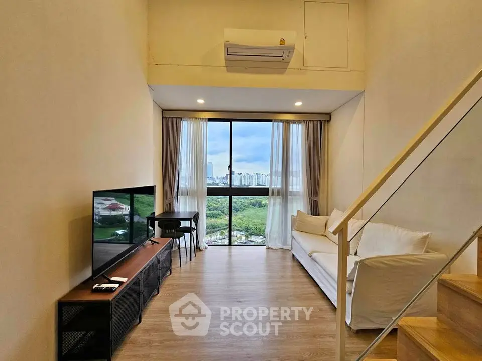 Modern living room with large window and scenic view, featuring cozy seating and sleek TV setup.