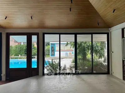 Spacious living room with large glass doors opening to a poolside view, featuring modern ceiling lights and wooden accents.