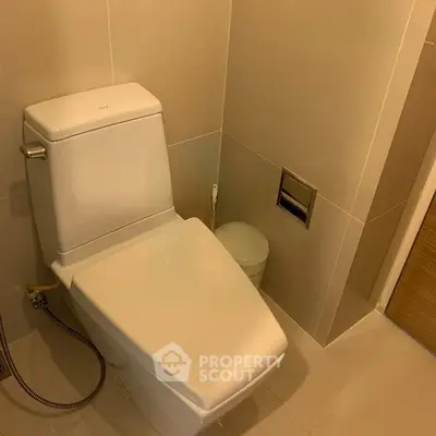 Modern bathroom with sleek toilet and beige tiles, offering a clean and minimalist design.