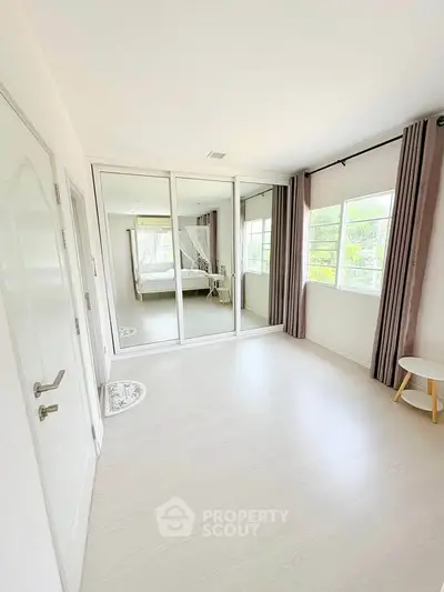 Spacious bedroom with mirrored closet doors and large windows offering natural light.