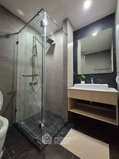 Modern bathroom with glass shower and sleek vanity in contemporary apartment.