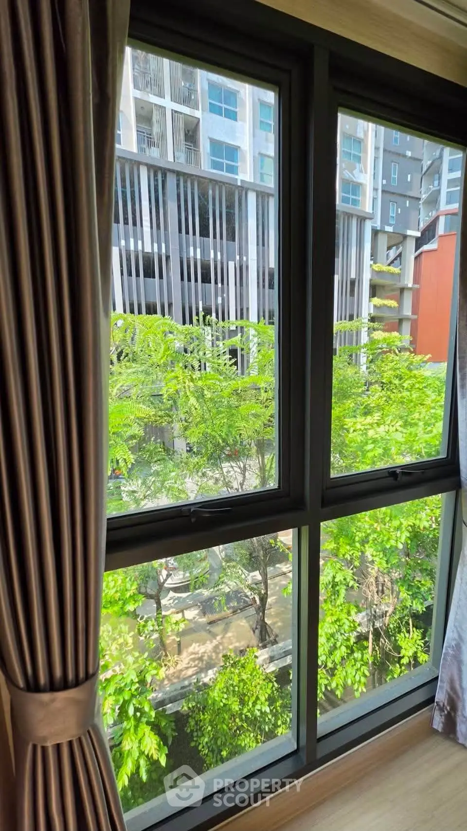 Bright window view of modern apartment with lush greenery and urban architecture.