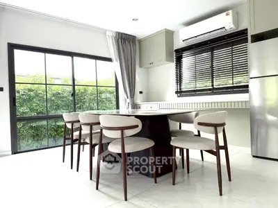 Modern dining area with sleek furniture and large windows offering lush garden views.
