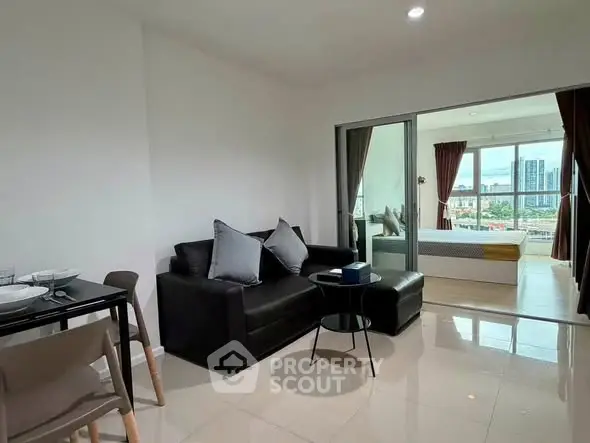 Modern open-plan living room with sleek black sofa and city view from balcony.