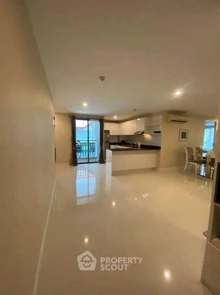 Spacious open-plan living room with modern kitchen and dining area, featuring sleek flooring and ample natural light.