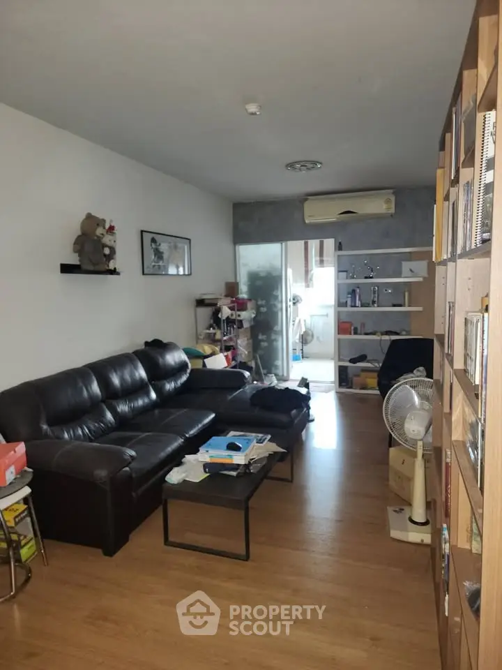 Cozy living room with leather sofa and wooden flooring, leading to a compact kitchen.