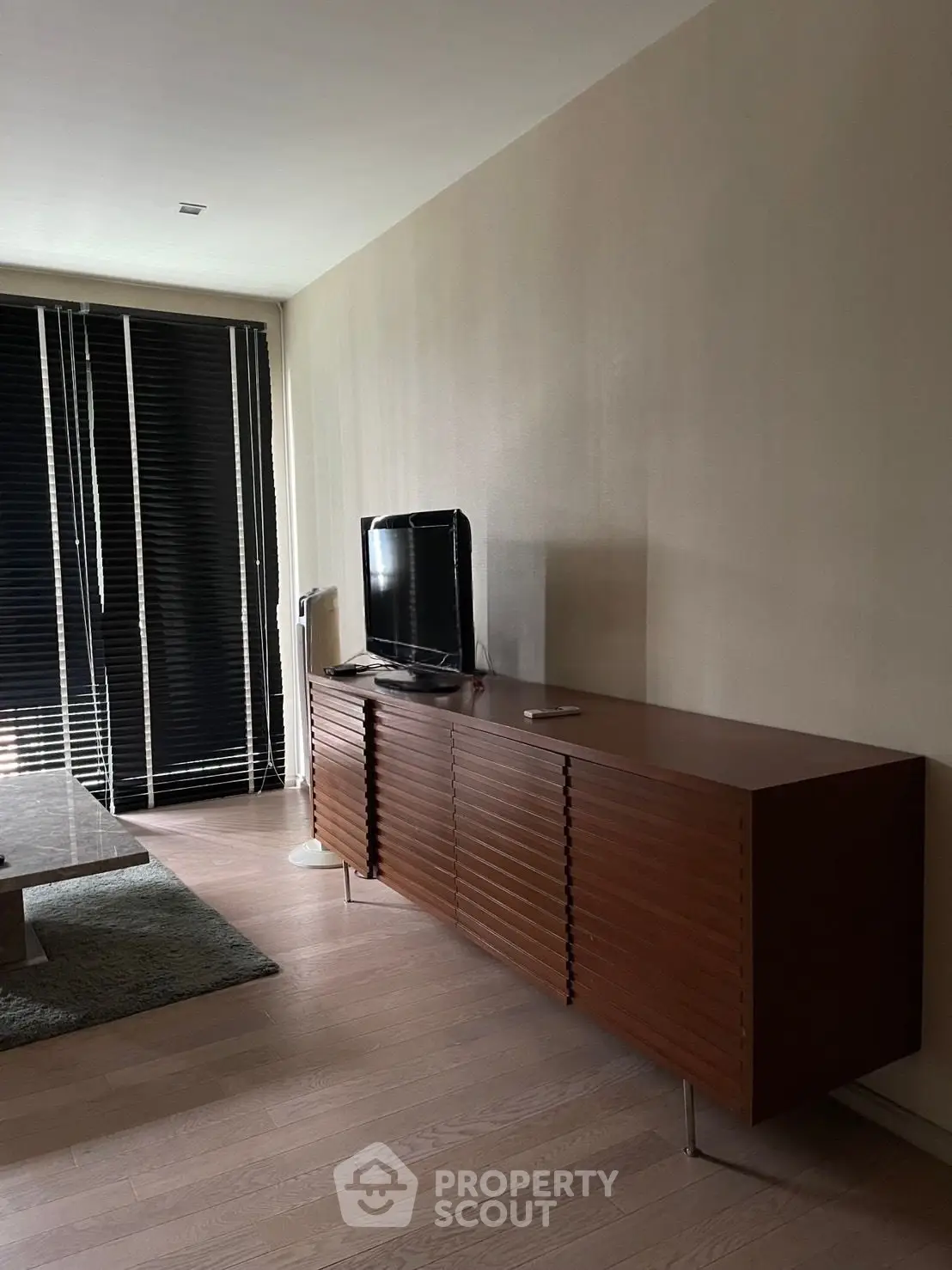 Modern living room with sleek wooden cabinet and flat-screen TV, featuring stylish blinds and minimalist decor.